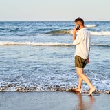Ein Mann läuft mit einem Hndy am Ohr am Strand entlang.