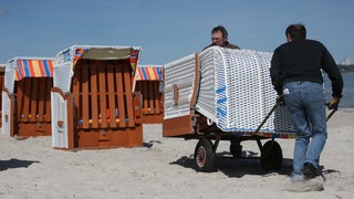 Zwei Männer bauen Strandkörbe auf.