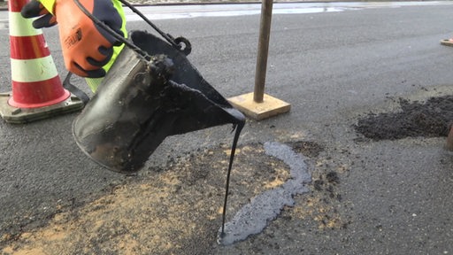 Bitumen wird in ein Loch in der Straße gegossen.