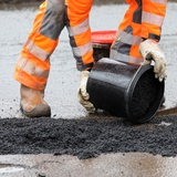 Ein Bauarbeiter schüttet Asphalt auf.