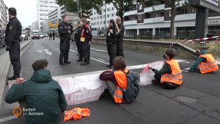 Aktivisten blockieren die Straße vor der Hochstraße am Bremer Hauptbahnhof mit Bannern.