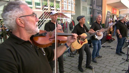 Zu sehen sind Straßenmusiker, die auf der Straße musik Spielen.