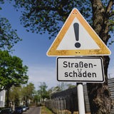 Ein Schild weist hin auf Straßenschäden an einer kaputten Straße.
