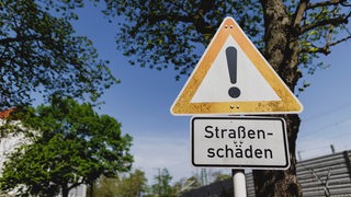 Ein Schild weist hin auf Straßenschäden an einer kaputten Straße.