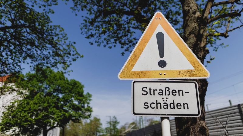 Ein Schild weist hin auf Straßenschäden an einer kaputten Straße.