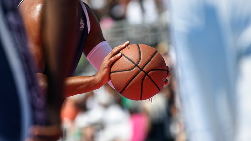 Ein Mann hält einen Basketball in beiden Händen und bereitet sich auf einen Wurf vor.
