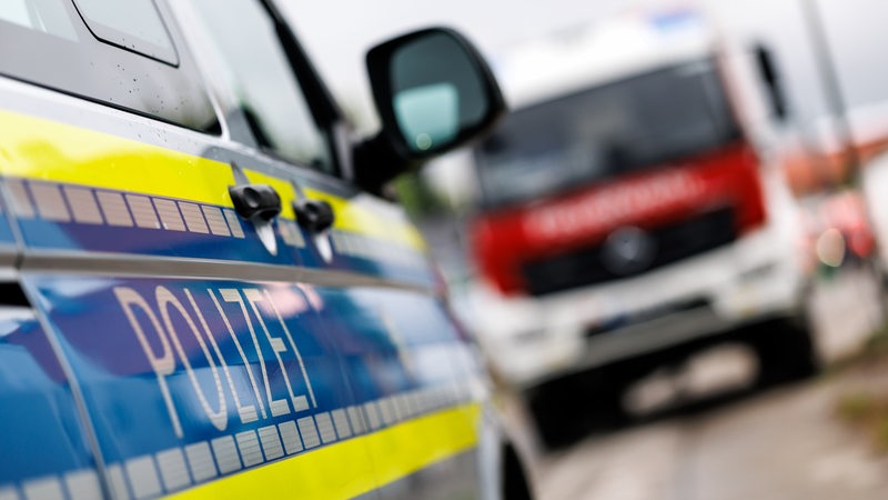 Der Schriftzug Polizei an einem Einsatzfahrzeug, im Hintergrund steht ein Einsatzfahrzeug der Feuerwehr.