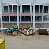Eine leere Baustelle ohne Menschen. Im Vordergrund ist ein Container zu sehen sowie Bau-Materialien.