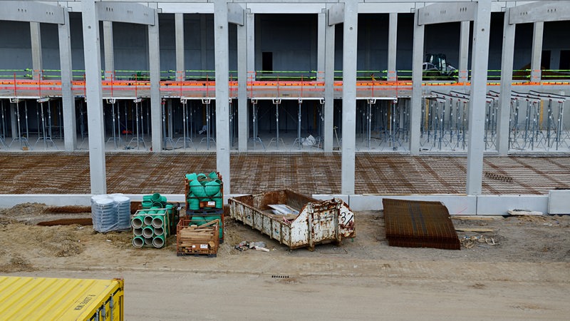 Eine leere Baustelle ohne Menschen. Im Vordergrund ist ein Container zu sehen sowie Bau-Materialien.