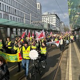 Streikende Menschen mit Transparenten und Fahnen ziehen am Bahnhof vorbei