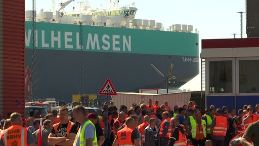 Streikende Hafenarbeiter vor einem Containerschiff.