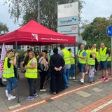 Menschen in gelben Warnwesten stehen an einem Pavillon.