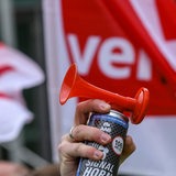 Eine Hand hält eine Fanfare in die Luft, im Hintergrund zwei Verdi-Fahnen