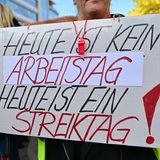 Streikende Arbeitnehmer*innen halten ein Plakat mit der Aufschrift: "Heute ist keine Arbeitstag - Heute ist Streiktag!" in den Händen.