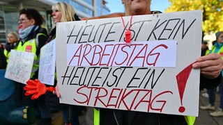 Streikende Arbeitnehmer*innen halten ein Plakat mit der Aufschrift: "Heute ist keine Arbeitstag - Heute ist Streiktag!" in den Händen.