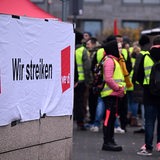 Hinter einem Transparent mit der Aufschrift: "Wir streiken/Verdi", stehen in gelben Warnwesten streikende Menschen.