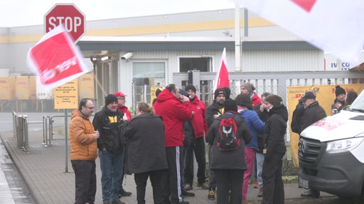 Mehrere Menschen demonstrieren mit Verdi-Fahnen vor einem DHL Gebäude.