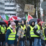 Menschen in gelben Warnwesten laufen in einem Demonstrationszug durch die Straßen und streiken.
