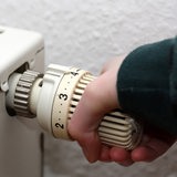 Eine Hand dreht einen Heizkörper auf.