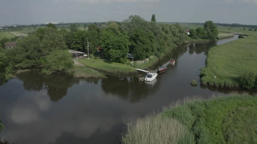Eine Drohnenaufnahme von der Ochtum in Bremen Strom. An einem Anleger liegen drei Schiffe im Wasser.