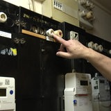 Eine Hand zeigt auf ein Modul an einer Wand mit Stromzählern.