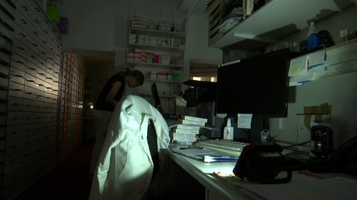 Es ist ein dunkles Büro zu sehen, in welchem ein Lichtstrahl einer Taschenlampe einen Schreibtisch und einen Stuhl beleuchtet.
