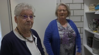 Die beiden Frauen Erika Habekost und Annegret Fischer-Böntgen in einem Raum mit Willkommensgeken für Neuankömlinge.