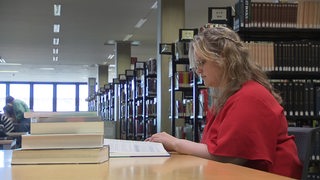 Eine Studentin sitzt an einem Tisch voller Bücher und lernt in der Bibliothek der Universität Bremen. 