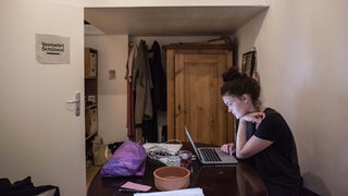 Eine Studentin sitzt in ihrem WG-Zimmer und lernt an ihrem Laptop.