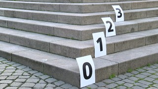 Graue Treppenstufen auf denen Zettel mit Nummern liegen.