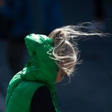 Eine Frau im im Wind, der Wind drückt ihre Kapuze gegen ihren Kopf, ihre Haare wehen.