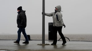 Zwei Menschen laufen bei Sturm einen Anleger entlang.