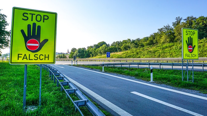 Zwei große Gelbe Schider mit der Aufschrift "Stop Falsch" stehen an einer Autobahnauffahrt.