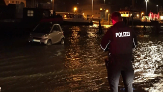 Ein Auto steht im Hochwasser, ein Polizist steht vor ihm.