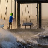 Ein Spaziergänger läuft bei Sturmflut und Wellen am Ufer der Wesermündung in Bremerhaven entlang.
