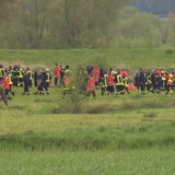 Menschen in Feuerwehruniform laufen in einer Kette durch eine Wiese