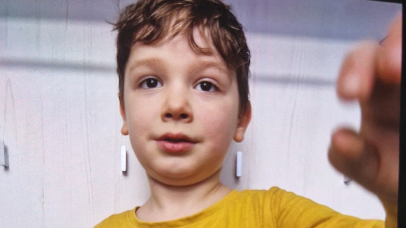 Ein kleiner Junge in einem gelben Hemd blickt in eine Kamera
