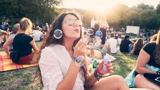 Junge Frau lässt Seifenblasen steigen auf dem Summer-Sounds-Festival