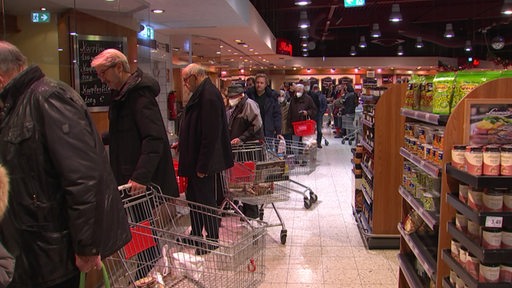 Viele Personen stehen mit Einkaufswagen in einer Schlange im Supermarkt.