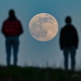 Menschen stehen auf einem Hügel und beobachten den aufgehenden Mond. 