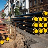 Ein Stapel neuer Rohre für Fernwärme liegt an einer Baustelle.