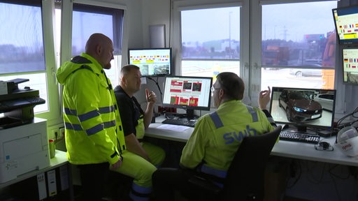 Drei Angestellte der SWB in ihrem Büroplatz mit Ausblick auf Wasser, LKW und Industrie.