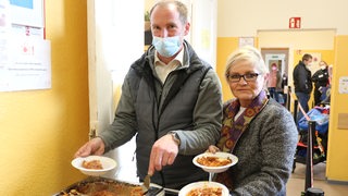 Eine Frau und ein Mann laden Essen auf Teller.