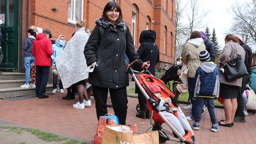Eine Frau mit Kinderwagen steht vor einem Gebäude.
