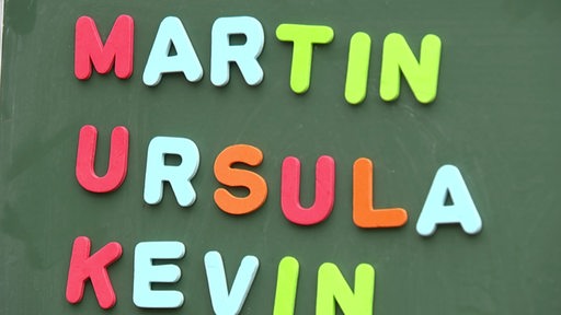 Die Namen "Martin, Ursula und Kevin" in bunten Magnetbuchstaben auf einer Tafel.