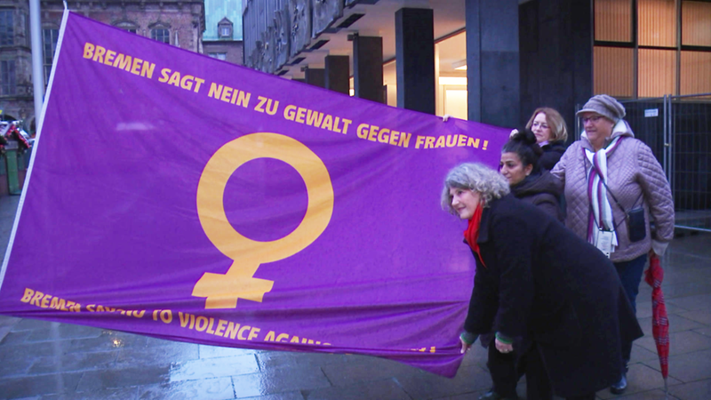 Mehrere Frauen halten eine Flagge, auf der Gewalt gegen Frauen verurteilt wird.