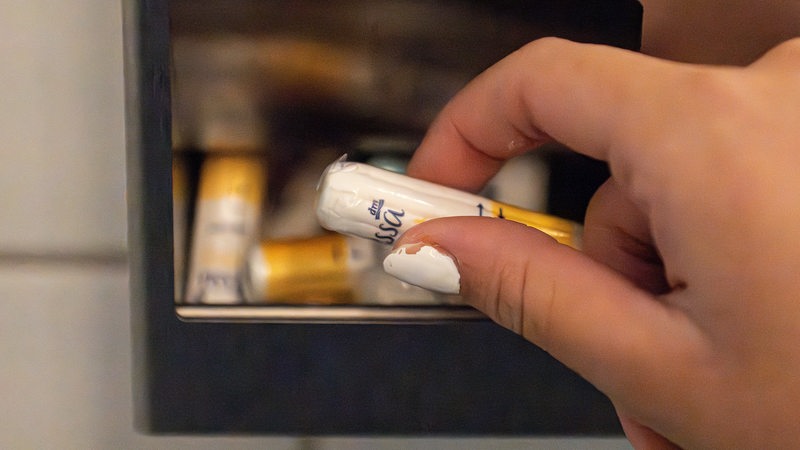 Eine Frau nimmt auf einer Toilette kostenlose Tampons aus einer Metallbox. 