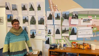Eine Frau steht vor einer Wand mit ausgedruckten Tannenbaum-Bildern.