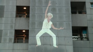 Eine Tänzerin wird auf eine Gebäudenwand projiziert.