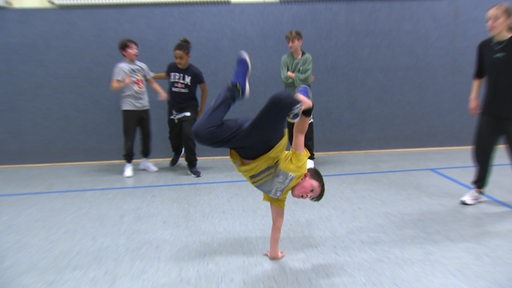 Ein Junge macht in einer Sporthalle einen Handstadt auf einer Hand. 